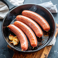Four smoked kielbasa links in a cast iron skillet.