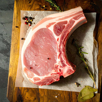 Single bone in pork chop on wooden cutting board.